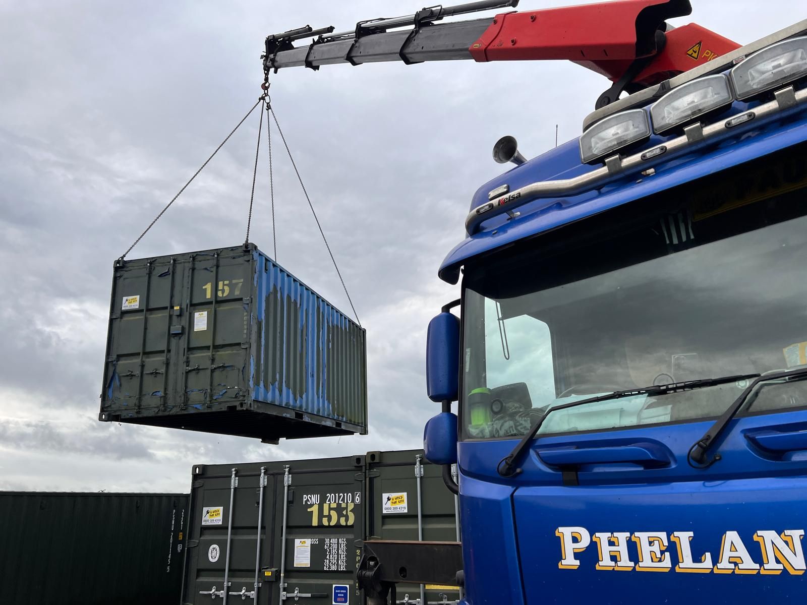 A used shipping container being lifted by a crane truck